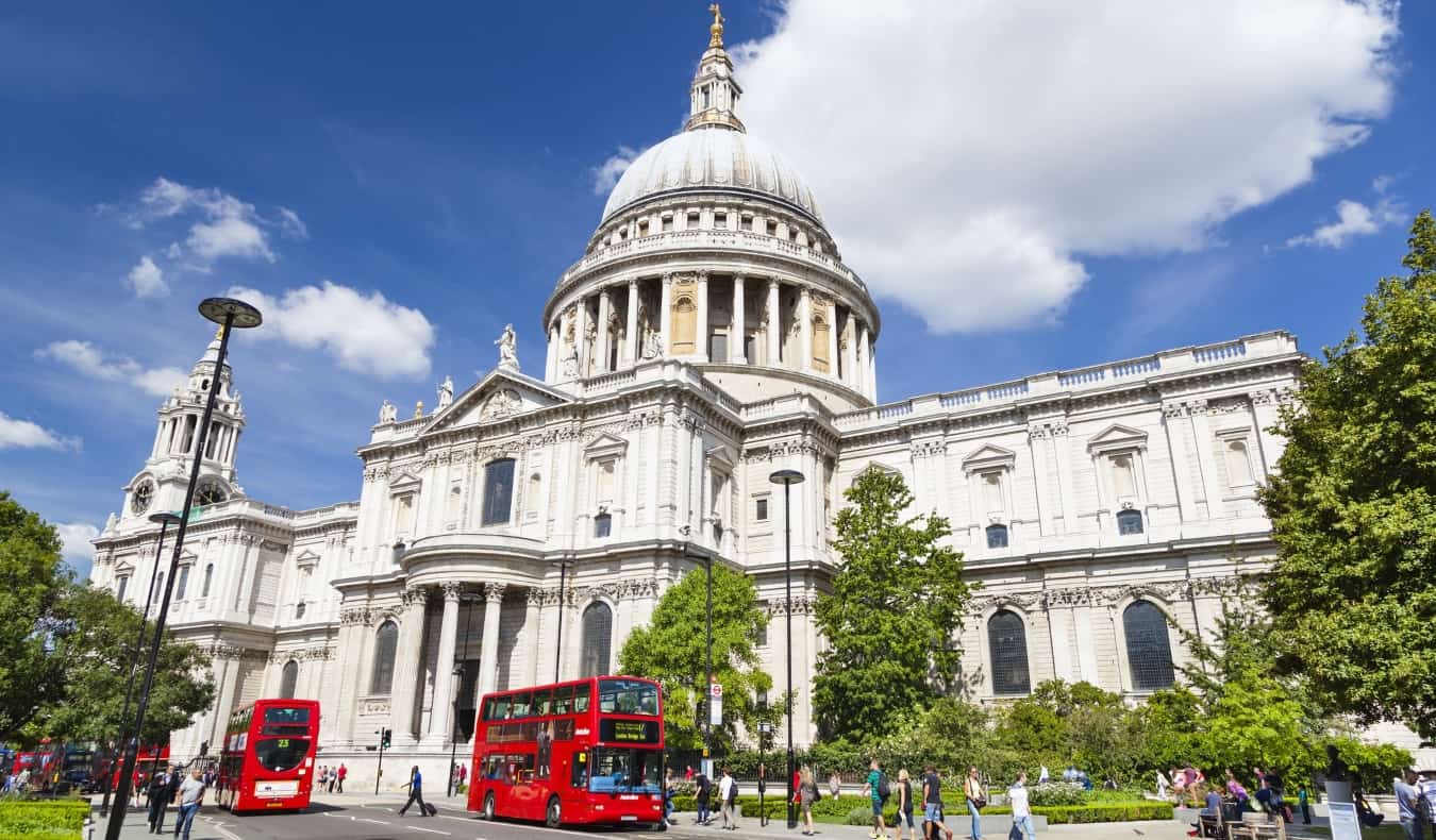 Front view of the domed St. Paul's cathedral, with double decker red buses and people walking in front of it in London, England